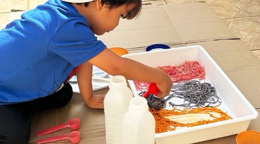 Menino explorando uma bandeja com macarrão colorido e potinhos