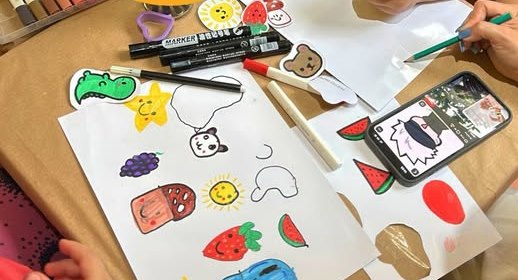 Mesa da oficina com desenhos coloridos de frutas, bichinhos e canetinhas